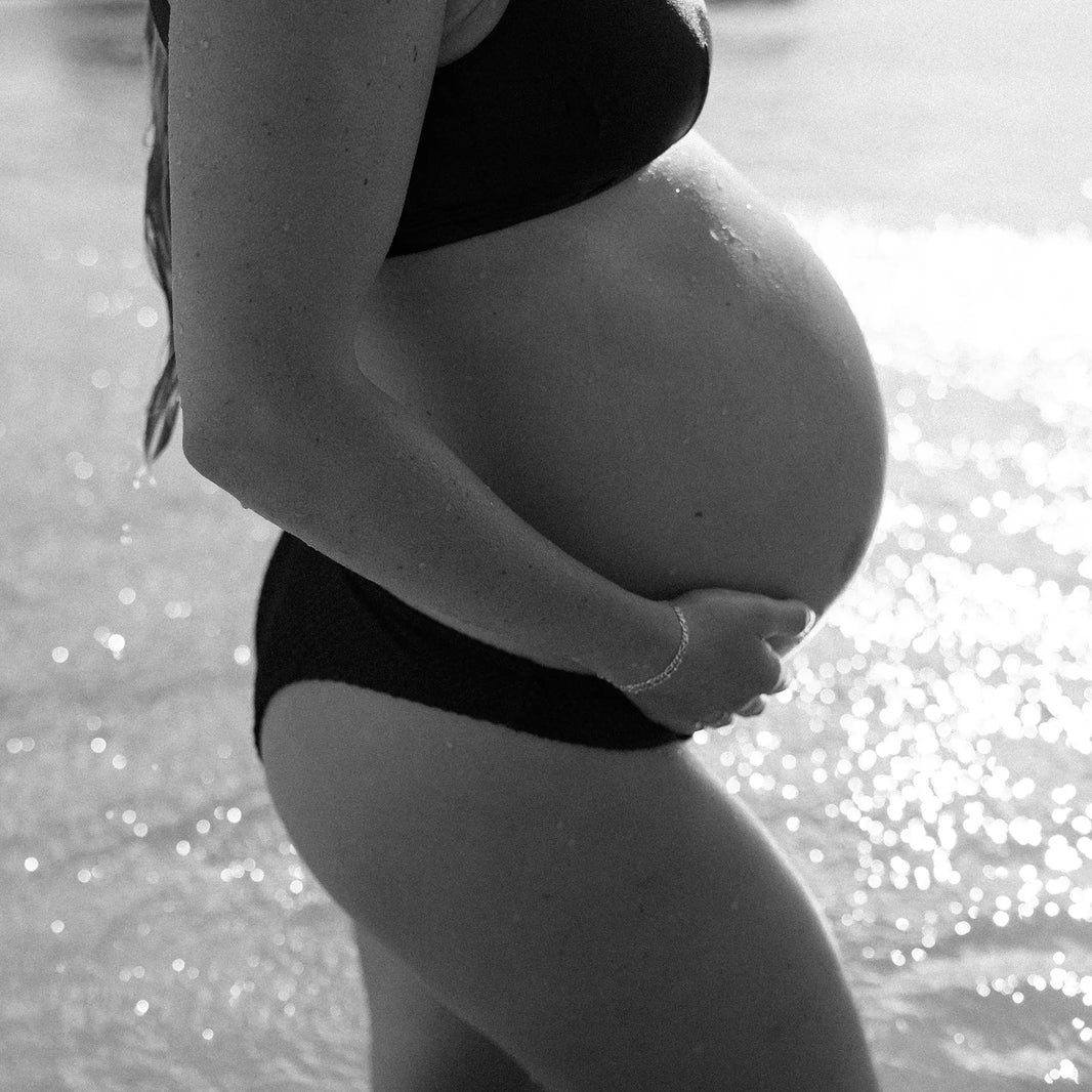 Momday pregnancy facts blog b/w photo of Ella holding her belly with water glistening in the background
