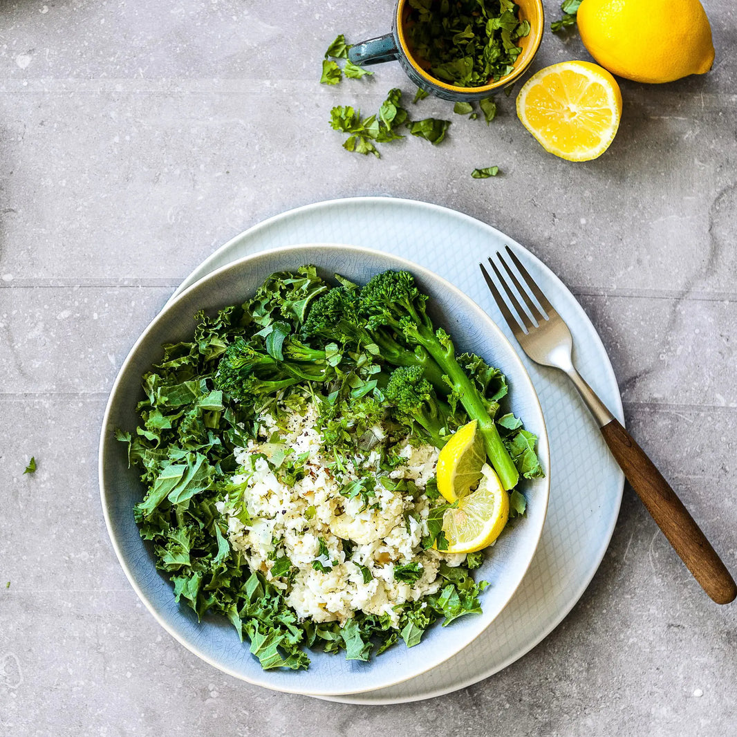 Momday pregnancy food blog photo of a bowl of broccolini, rice and kale with sliced lemon on the table.