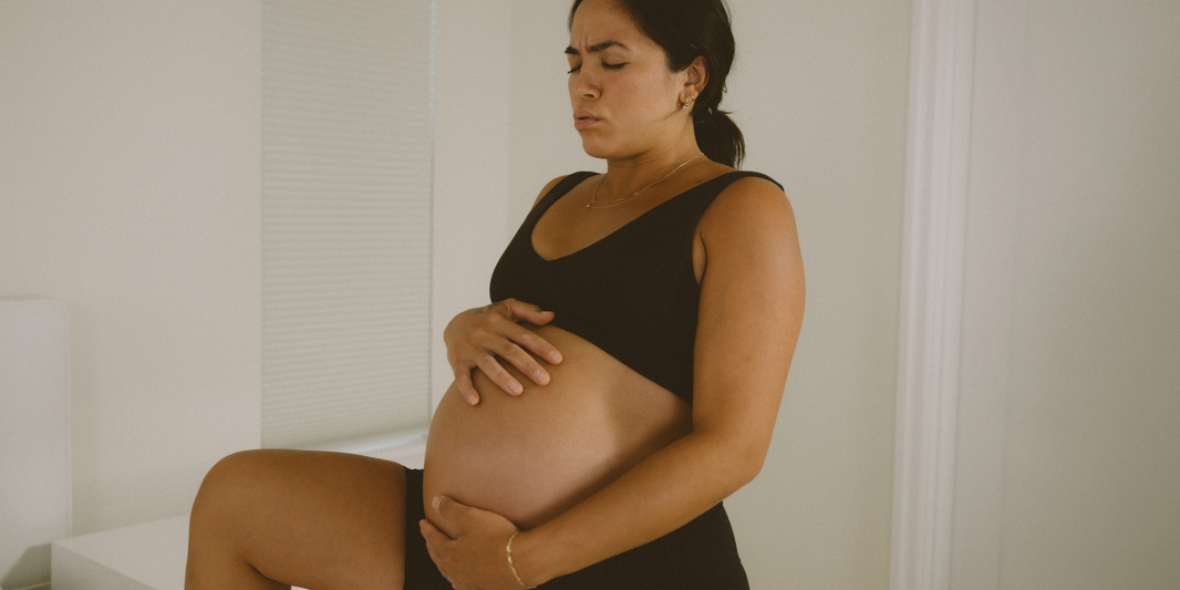 Pregnant mother holding her belly and doing a pregnancy workout in third trimester. This is to help prepare for pregnancy and the 3 stages of labor.