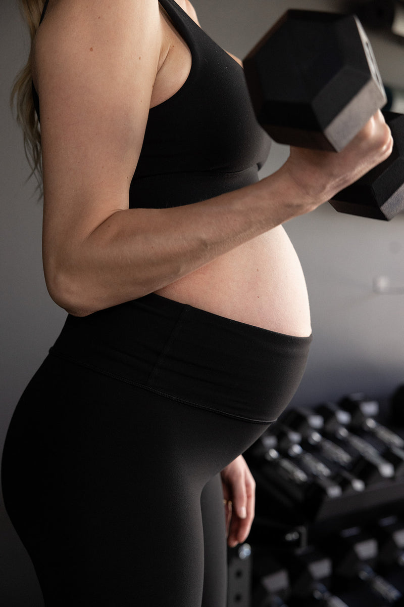 A side profile of early pregnancy fitness mom doing arm exercises and curling a dumbbell for trimester 2 workout program.